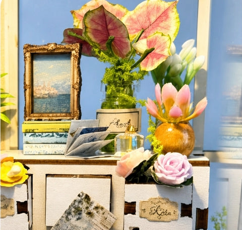 Kommode mit Blumen, Büchern, Briefen und gerahmtem Bild