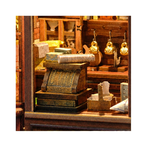 Verzierte Miniatur-Registrierkasse mit Papierrolle und goldfarbenen Tassen im Hintergrund